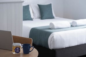 A neatly made bed with white and green bedding, a laptop, a mug, and a jar of cookies on a wooden table. - Central Motel Port Fairy (Port Fairy)