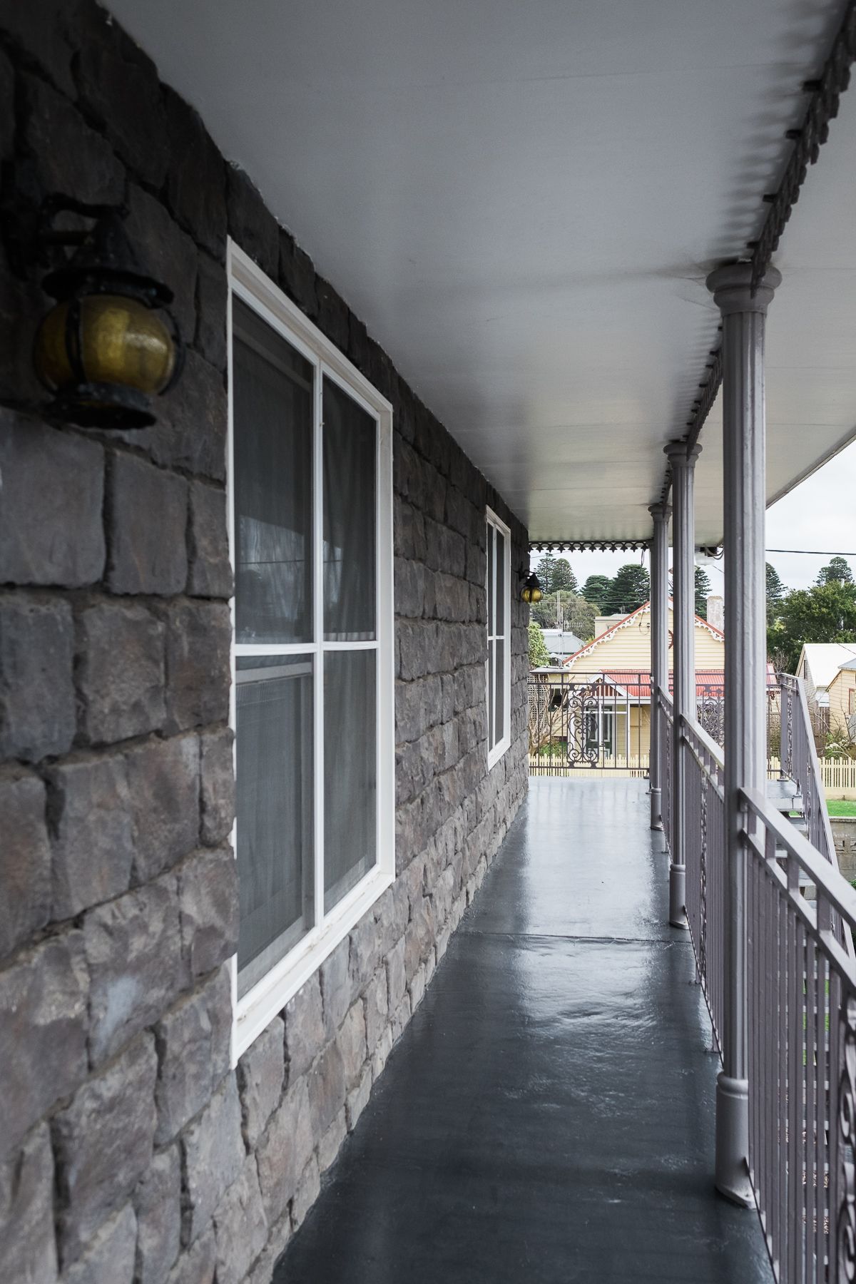 A covered porch with stone walls and large windows, leading to a view of a residential area.