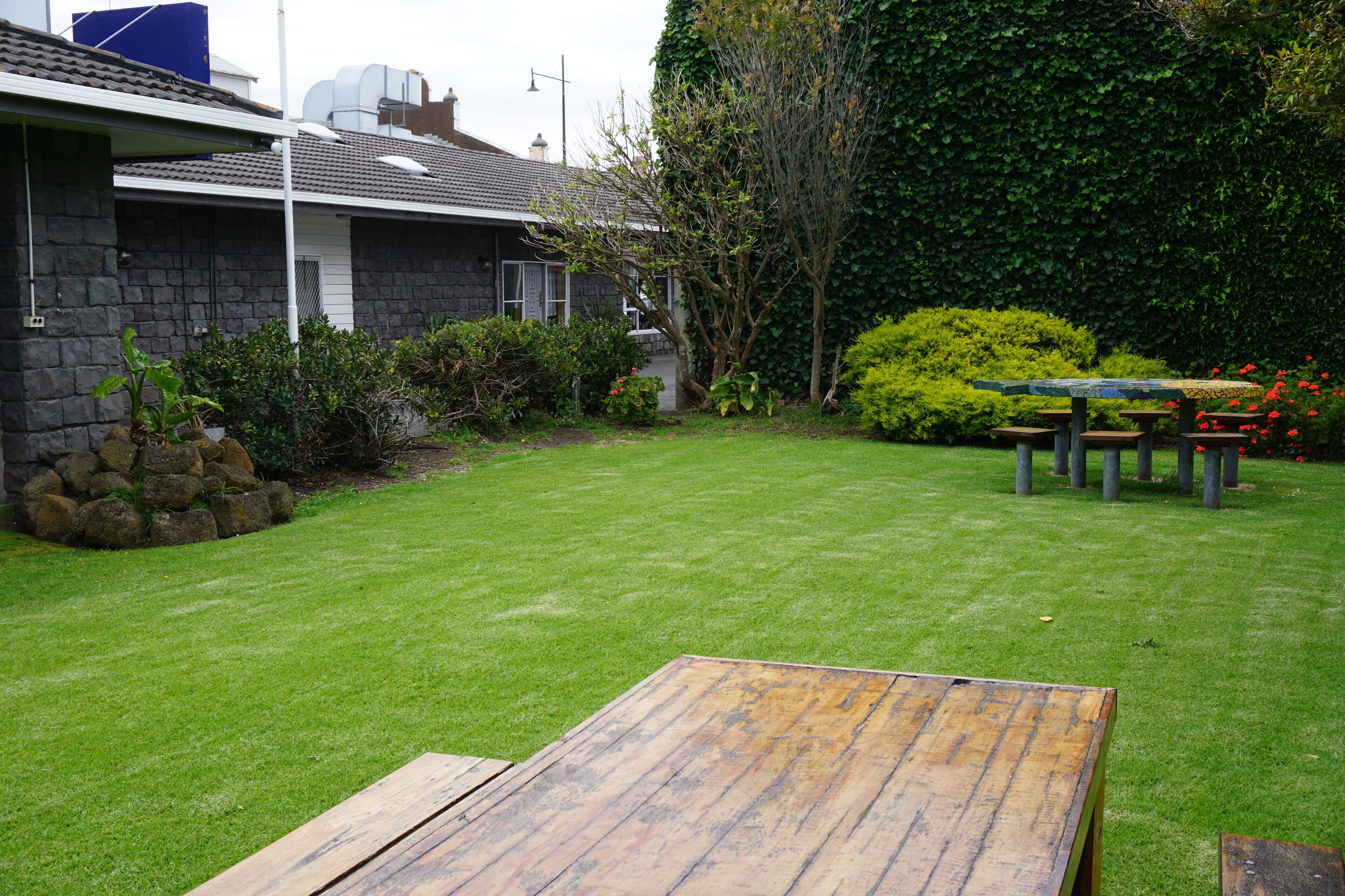 A residential property with a well-maintained lawn, a wooden deck, and a stone house with a tiled roof.