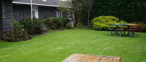 A residential property with a well-maintained lawn, a wooden deck, and a stone house with a tiled roof.