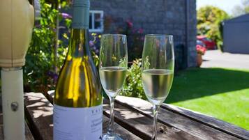 A bottle of wine and two glasses on a wooden table outdoors.