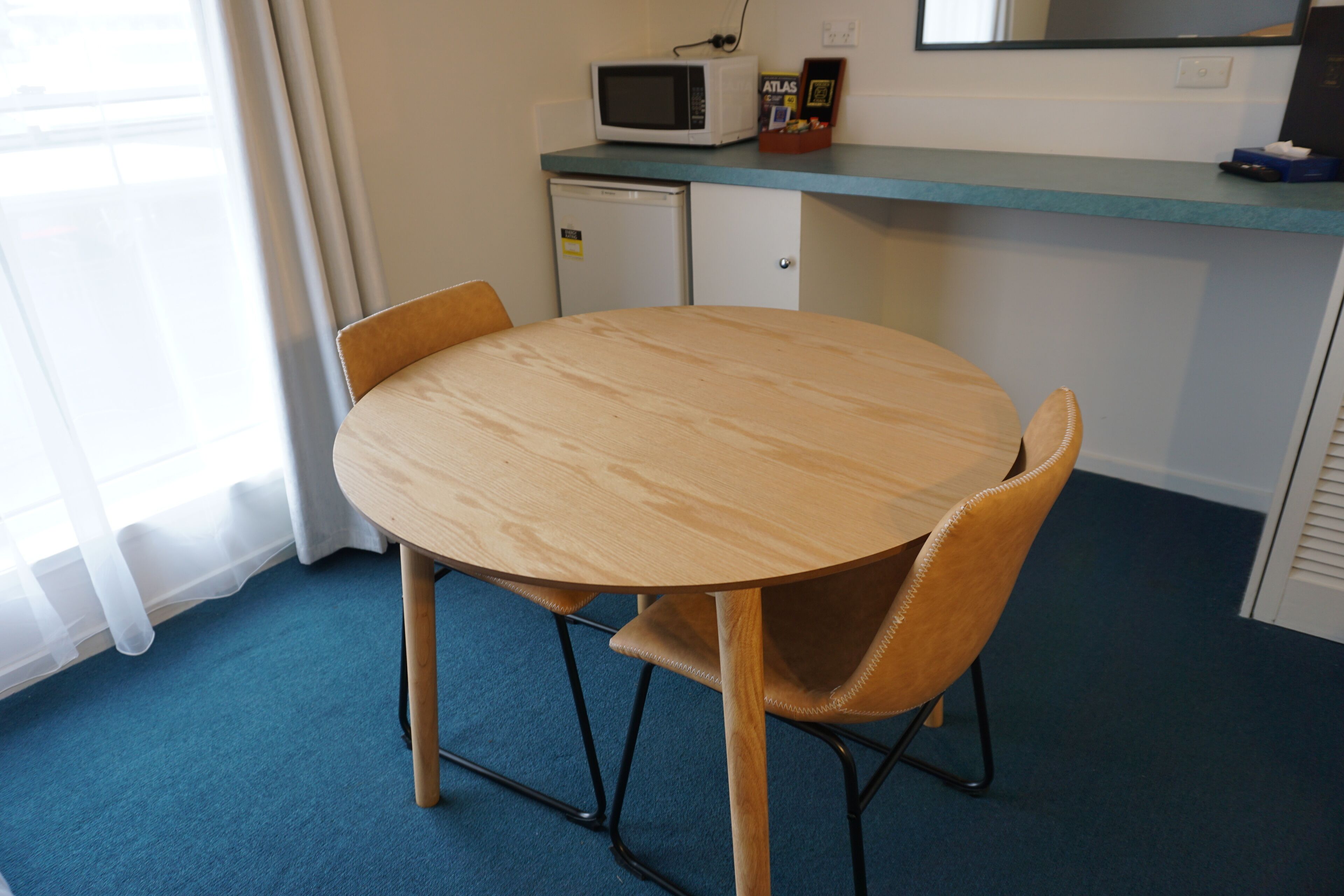 A small dining area with a round wooden table, two chairs, a microwave, and a small refrigerator.