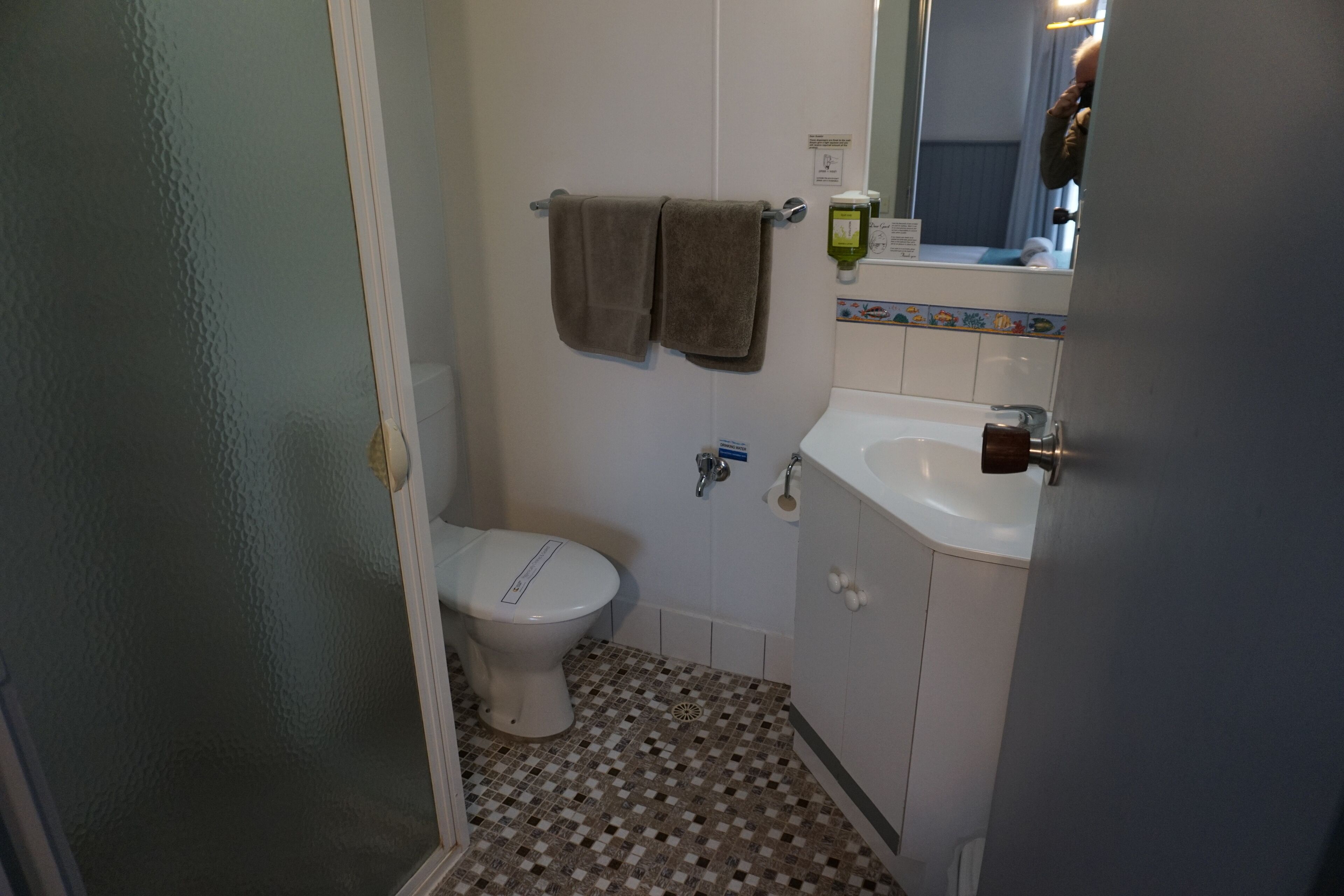 A small bathroom with a toilet, a sink, and a mirror. There are two towels hanging on the wall.
