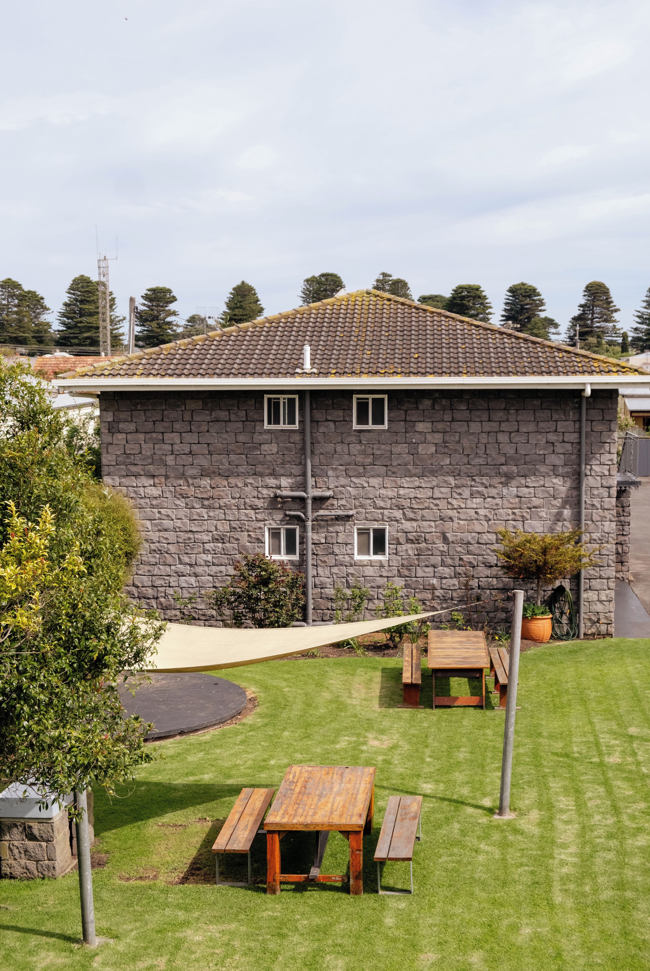 A stone building with a tiled roof, a grassy yard, and a picnic table.