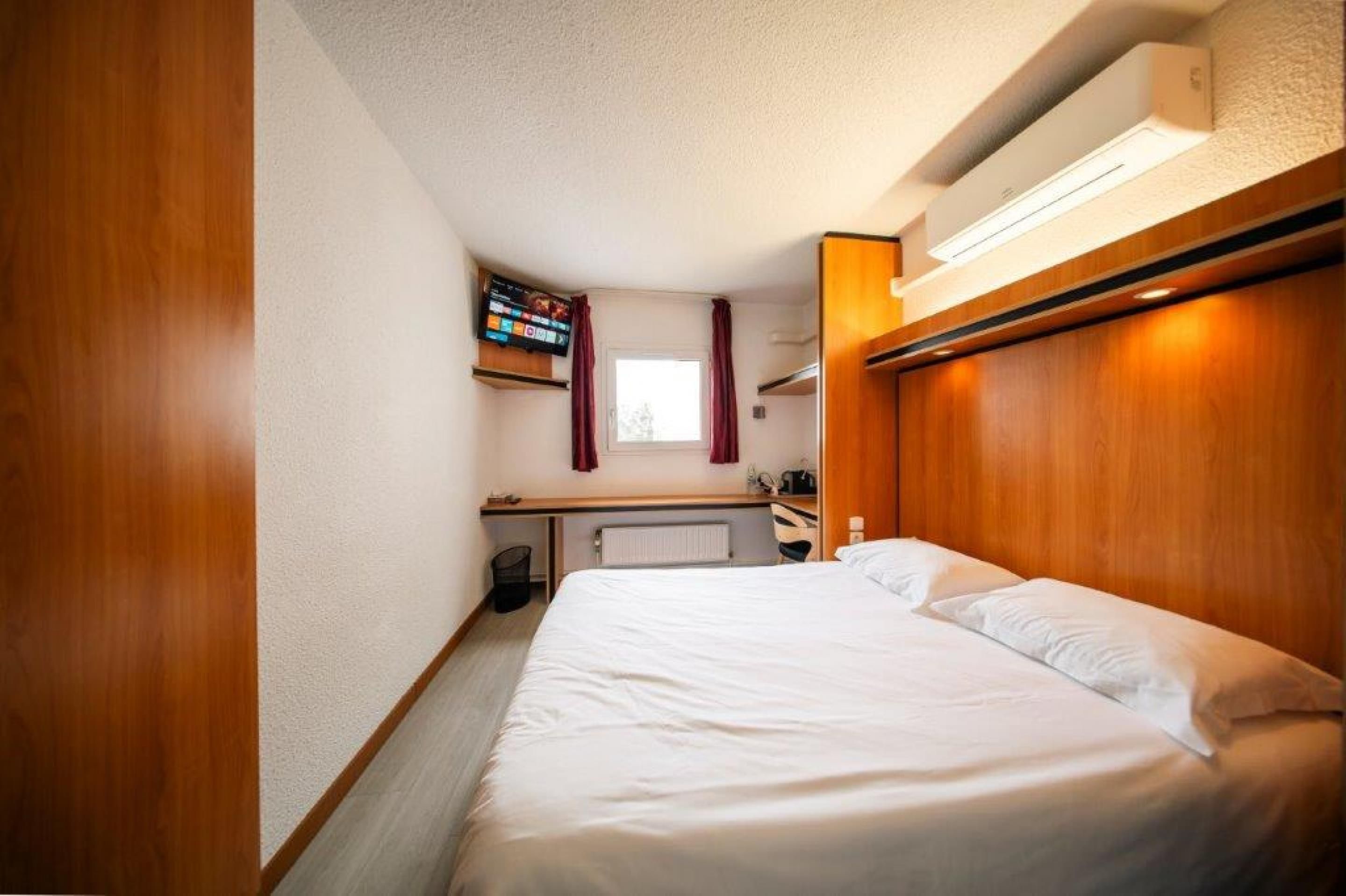Een hotelkamer met een bed, bureau, televisie en raam met gordijnen.