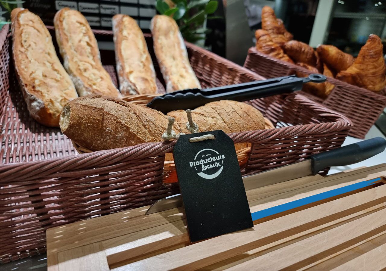 A display of baguettes and croissants in wicker baskets with a tag that reads "Producteurs Locaux."