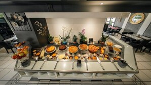 Montaje de bufé con diversos platos y utensilios, rodeado de plantas en macetas y elementos decorativos.