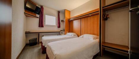 A hotel room with two beds, a TV, a window with curtains, and a wooden wardrobe.