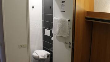 A hotel room with a bed, a wooden wardrobe, a white toilet, and a shower area.