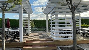 Un espace extérieur abrité, doté de pergolas blanches, d’un plancher en bois, de tables et de chaises.