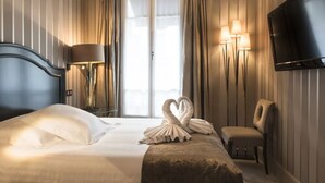 Una habitación de hotel con cama, televisión, sillón y ventana con cortinas.