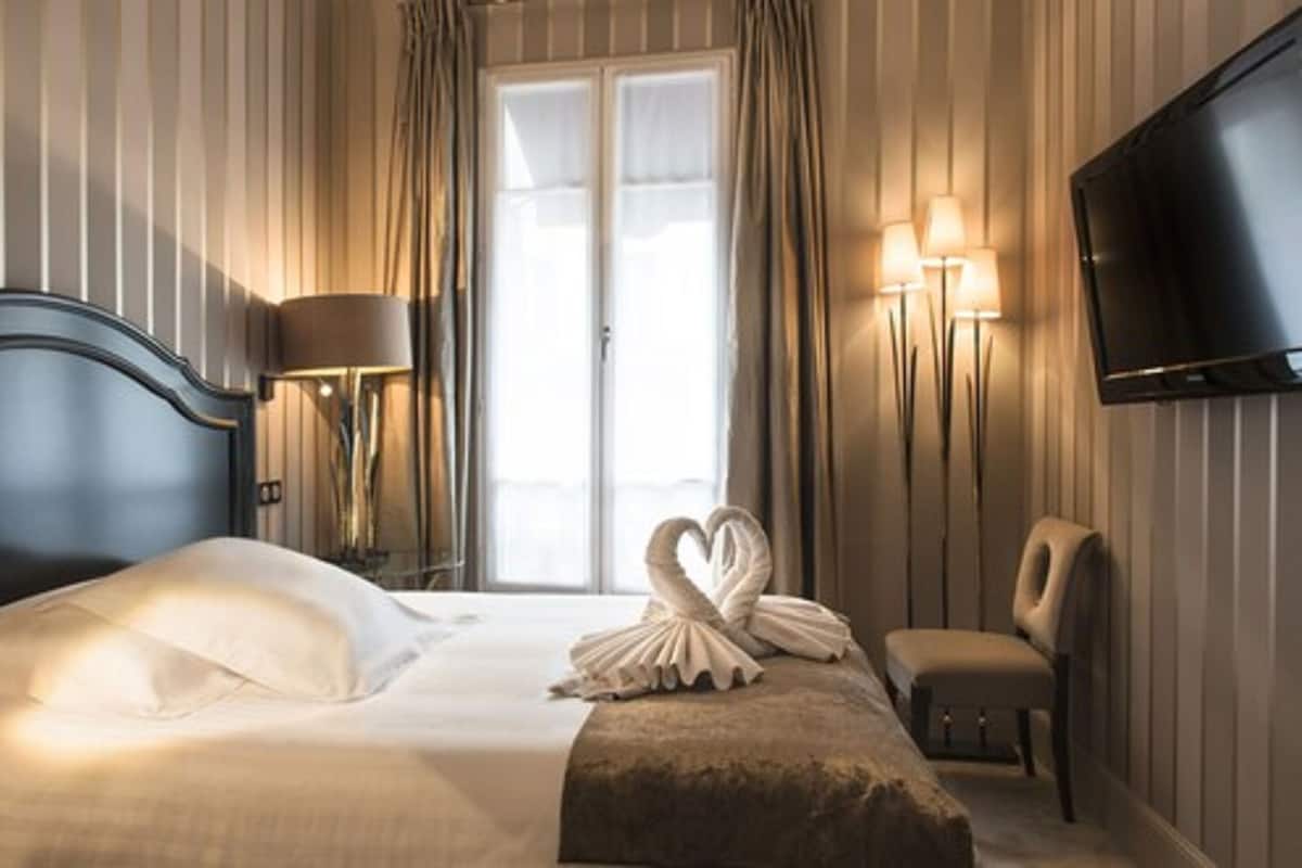 Una habitació d'hotel amb un llit, televisió, cadira i finestra amb cortines.