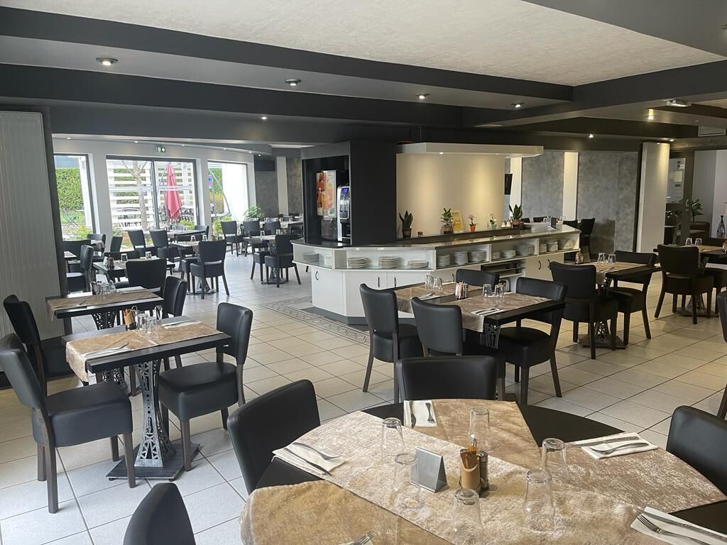 Un restaurante moderno con varias mesas y sillas, una zona de bar, y amplios ventanales con vistas al exterior.