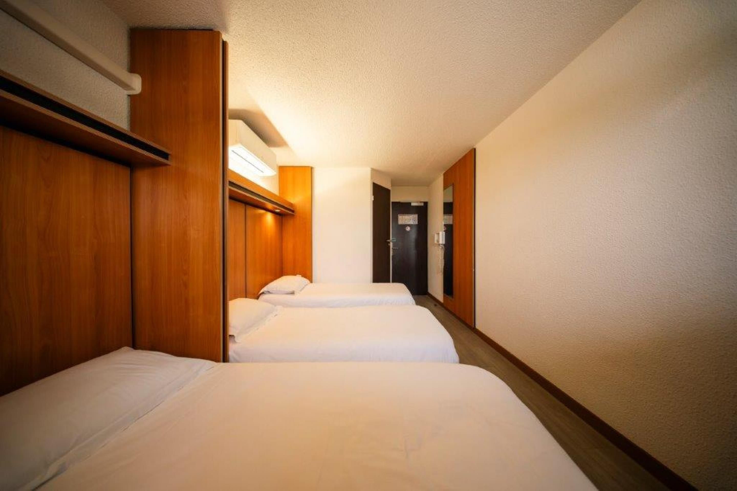 Habitación de hotel con dos camas, cabeceros de madera, un ventanal pequeño y una puerta que da a un baño.
