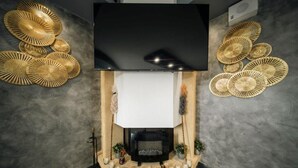 Una sala de estar moderna con un televisor de pantalla plana sobre una chimenea, rodeada de elementos decorativos en la pared y una fila de velas.