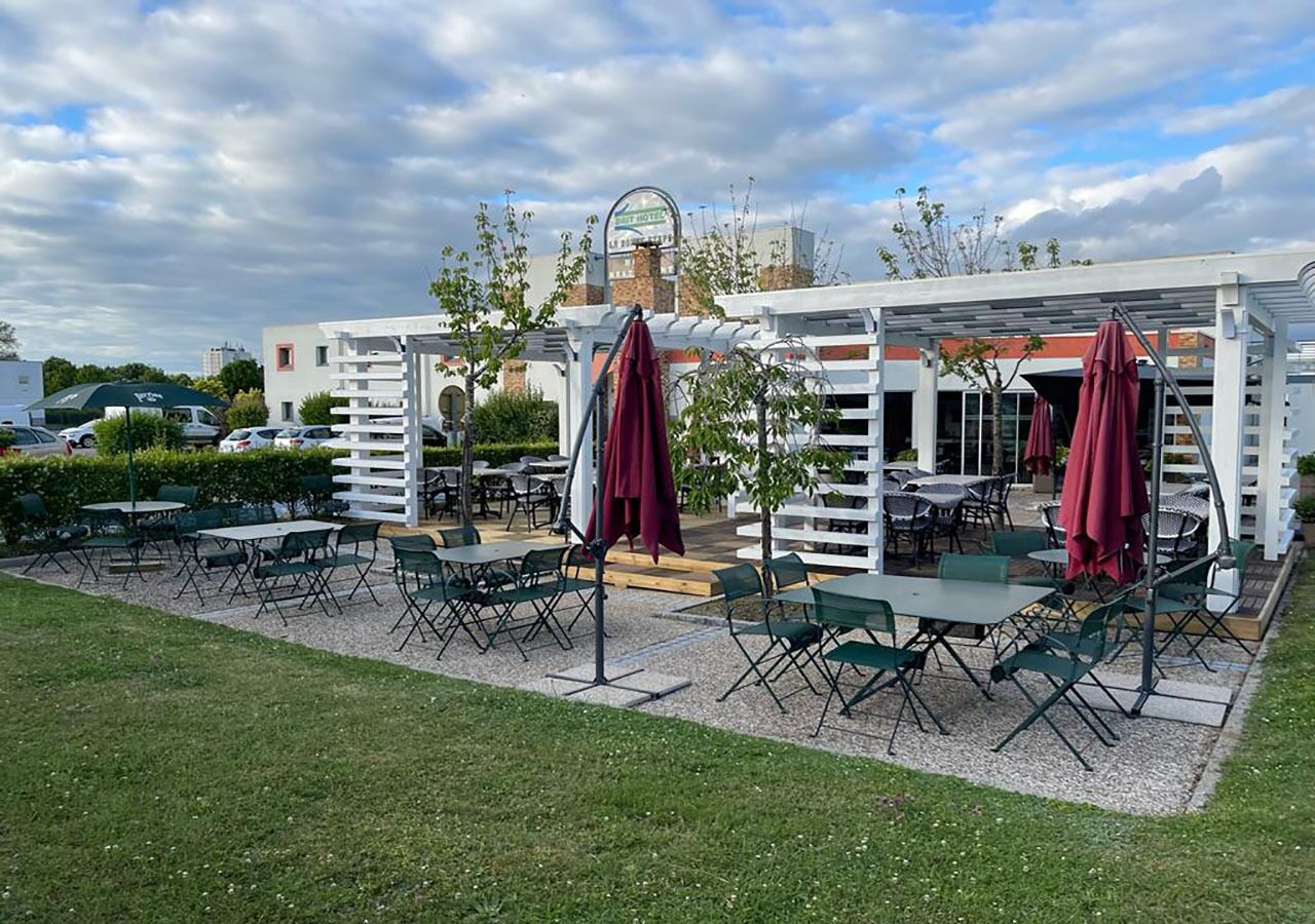 Un espace extérieur aménagé en terrasse, avec des tables et des chaises, une clôture blanche et un bâtiment en arrière-plan.