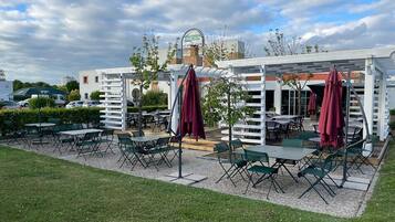 An outdoor patio area with tables and chairs, a white fence, and a building in the background.