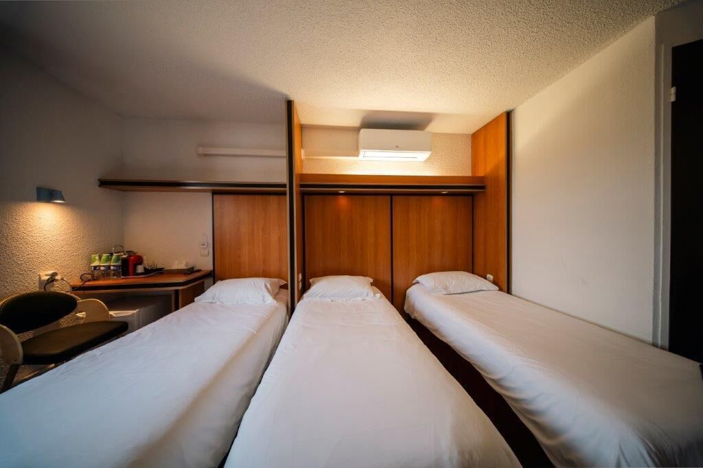 Een kleine hotelkamer met twee enkele bedden, een bureau met stoel, en een tafeltje met spullen erop.