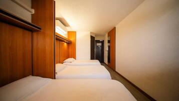 A hotel room with two beds, wooden headboards, and a hallway leading to a door.