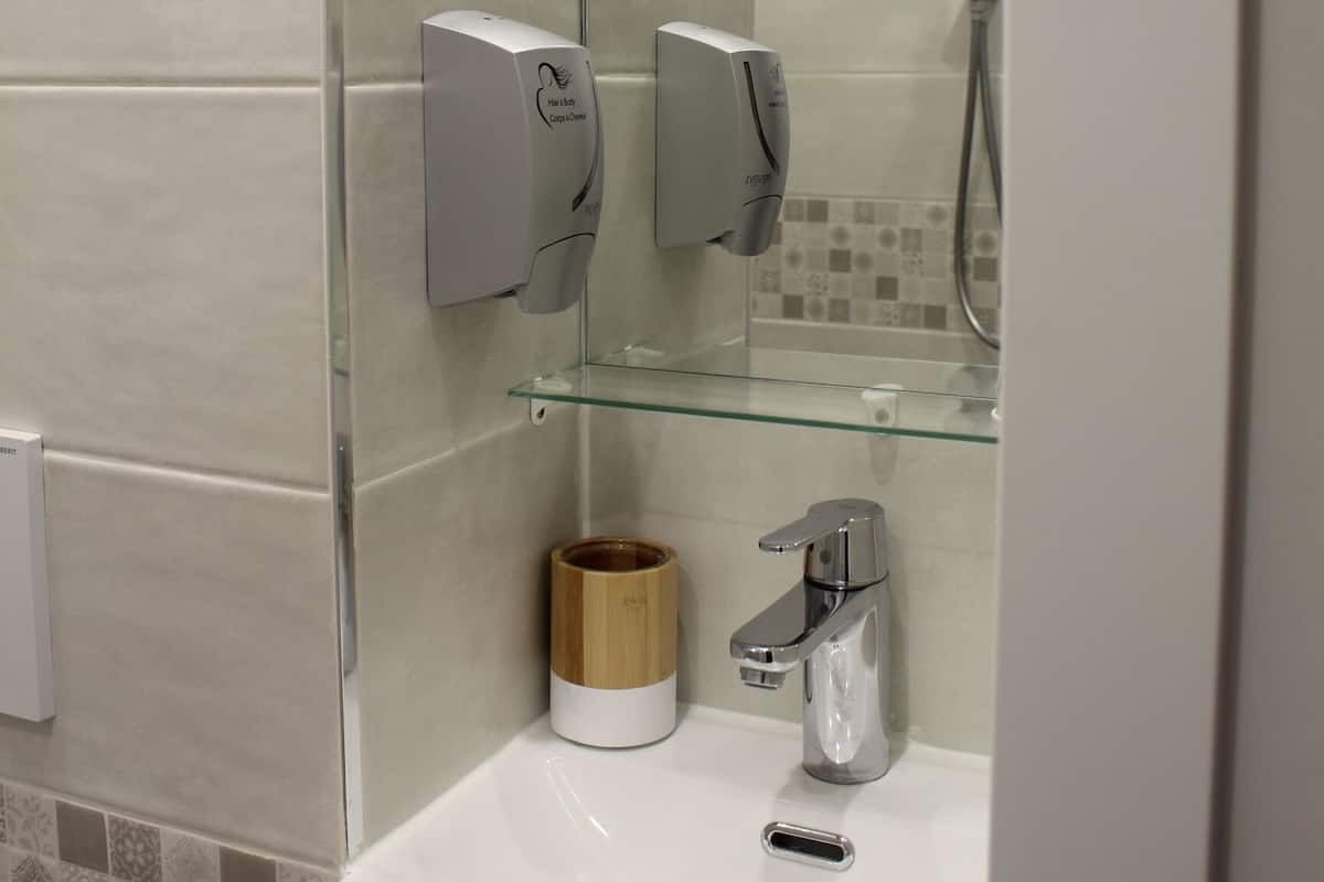 Un bany modern amb una dutxa de vidre, un lavabo blanc i un dispensador de sabó.
