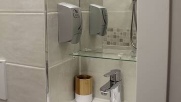 Een moderne badkamer met een glazen douchecabine, een wit wastafelmeubel en een zeepdispenser.