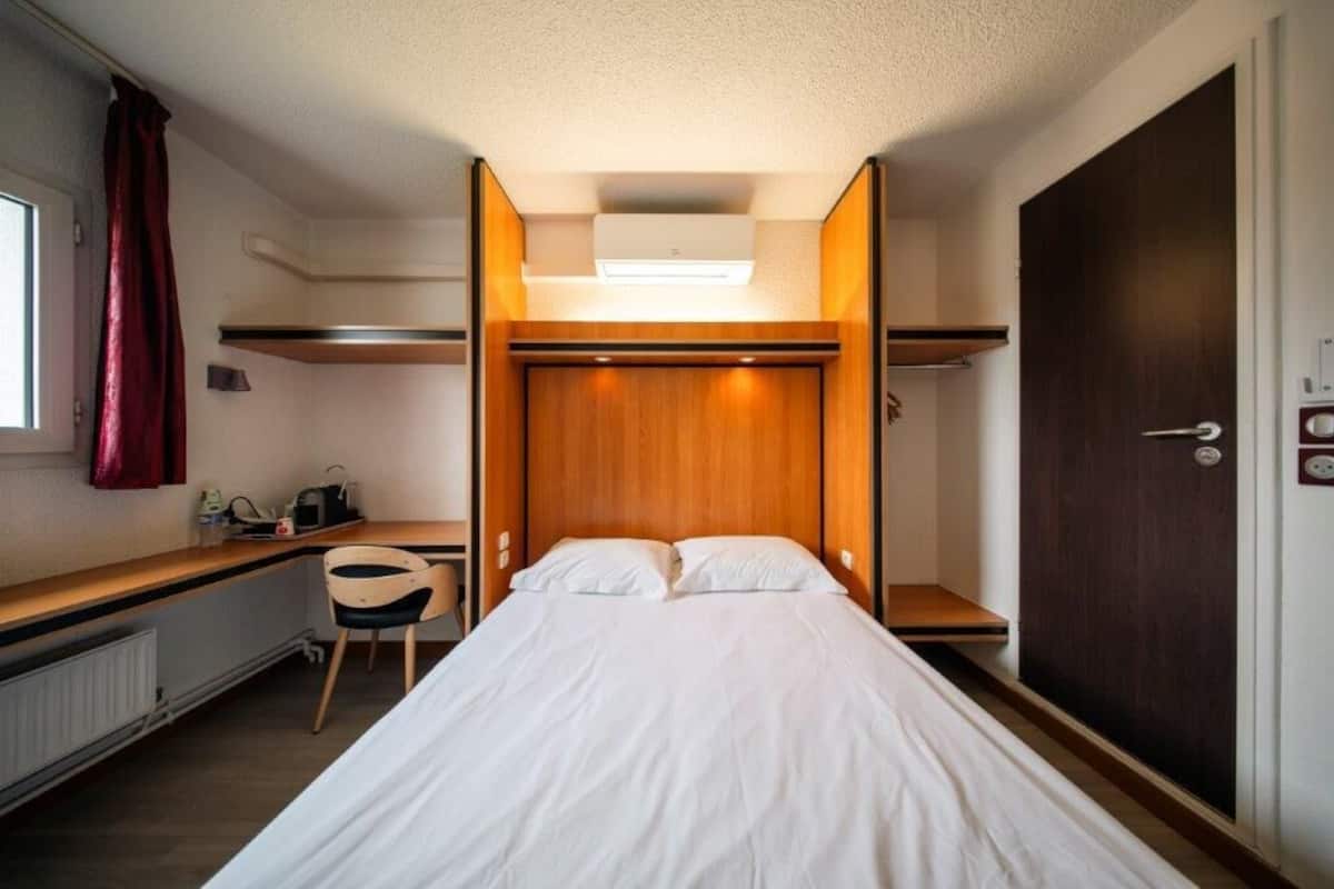Habitació d'hotel reduïda amb llit, escriptori i armari.