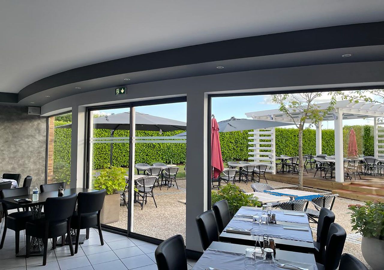 Un restaurant doté d’une salle à manger intérieure et d’une terrasse, de grandes fenêtres et offrant une vue sur le jardin.