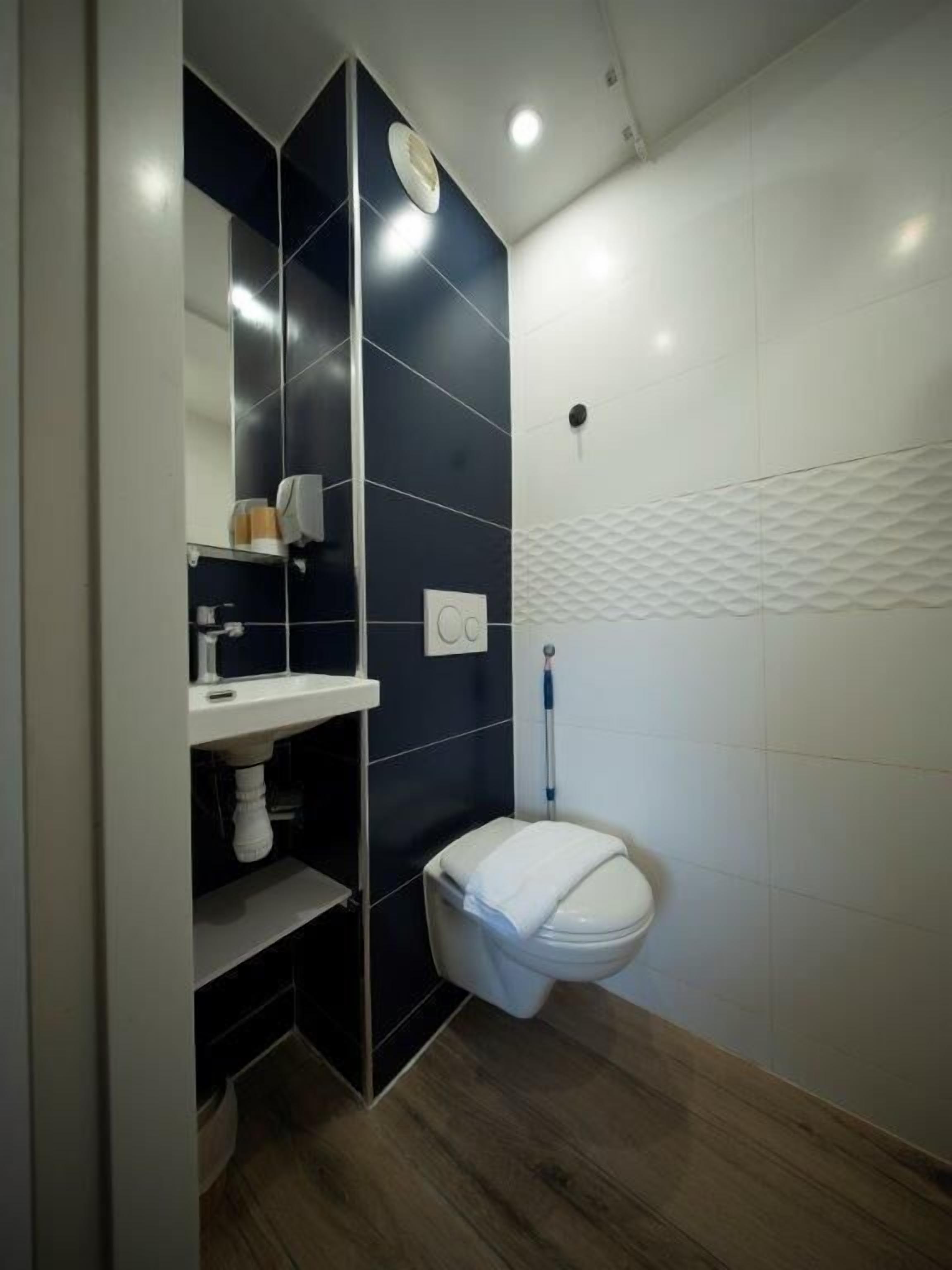 A modern bathroom with a dark tiled wall, a white toilet, and a wooden floor.