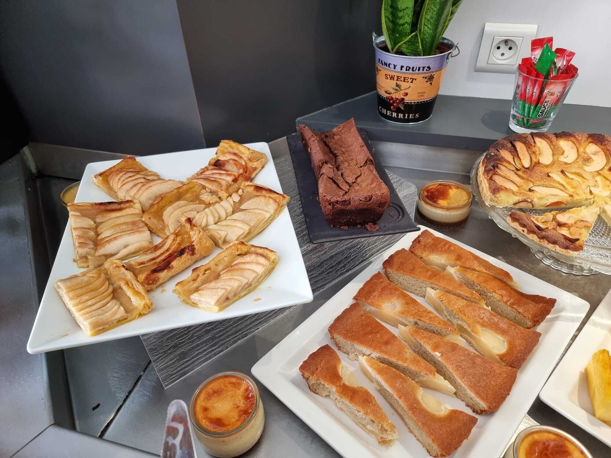 Une table de buffet proposant divers desserts, notamment une tarte aux pommes, un gâteau au chocolat et une tarte aux pommes en tranches.