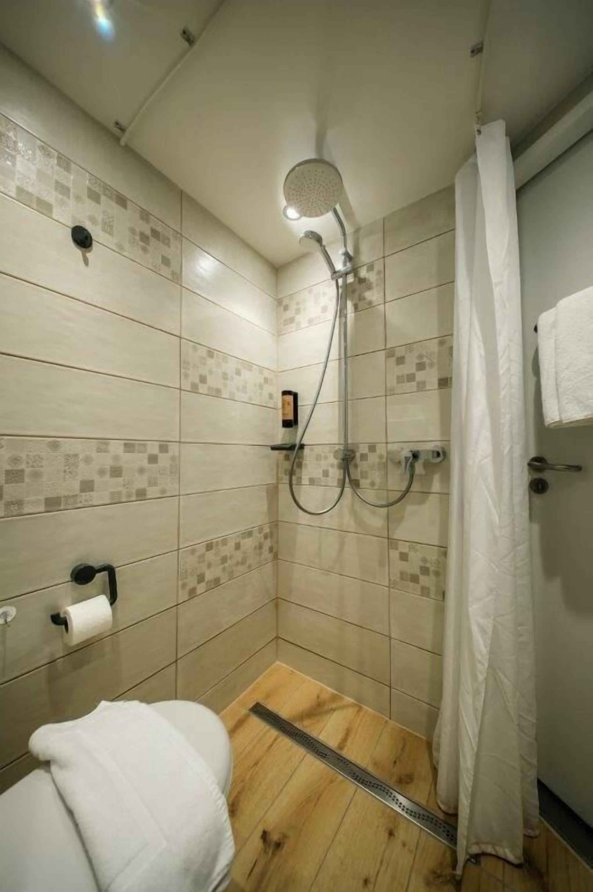 Une petite salle de douche carrelée, équipée d’un pommeau de douche à main, de toilettes et d’un porte-serviettes.