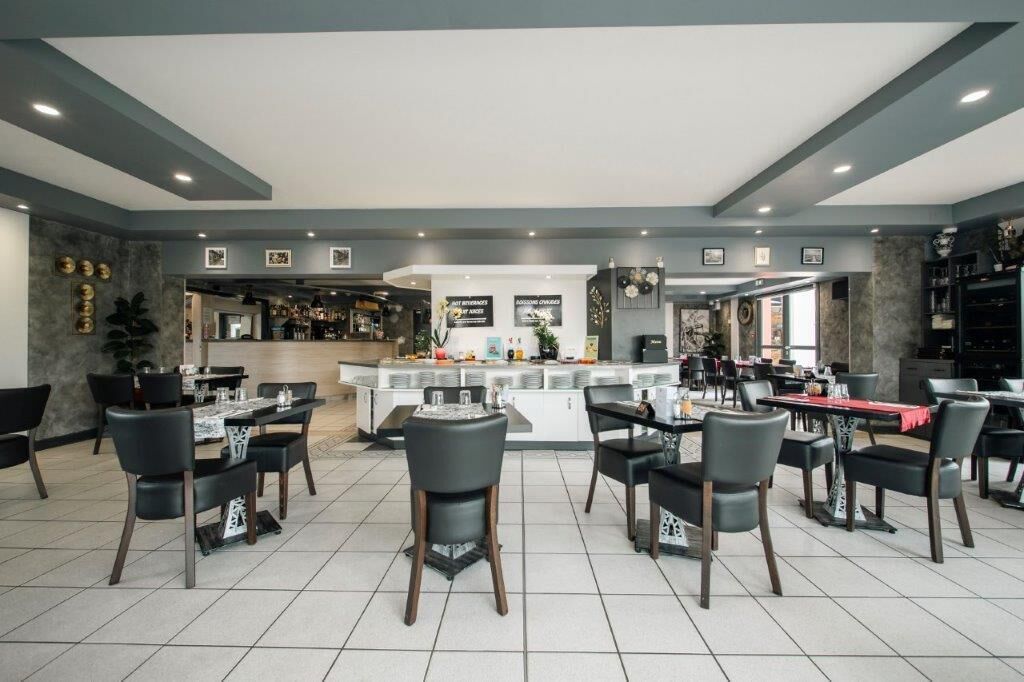 Ein modernes Restaurant mit einer zentralen Bar, mehreren Esstischen und schwarzen Stühlen.