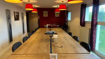 Una sala conferenze con un lungo tavolo, sedie, un proiettore e lampadari a sospensione rossi.