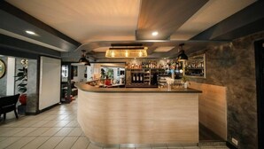 Un moderno bar con una barra curva, iluminación ambiental y una variedad de botellas y vasos en estanterías.