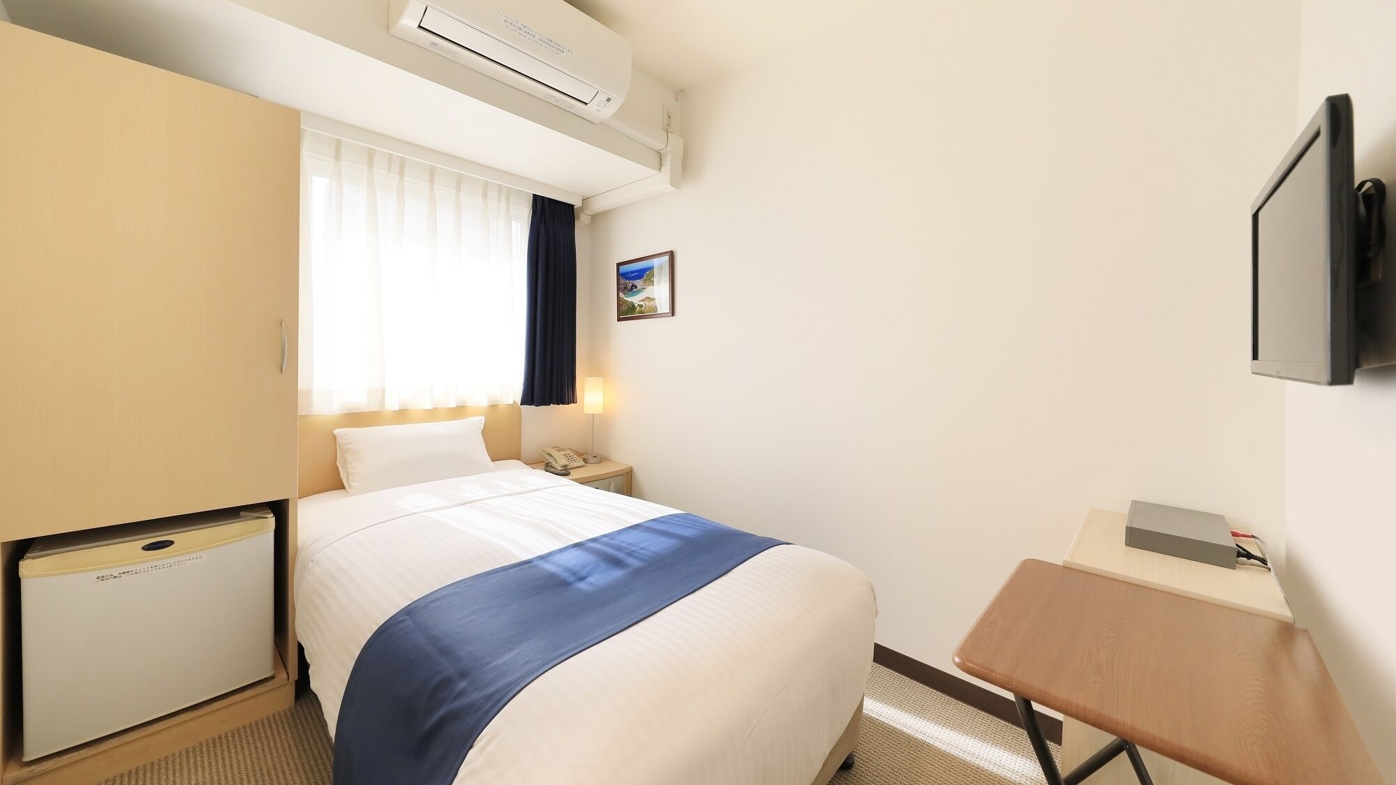 Habitació d'hotel amb llit, taulella de nit, làmpada, televisió, aparell d'aire condicionat i escriptori petit.