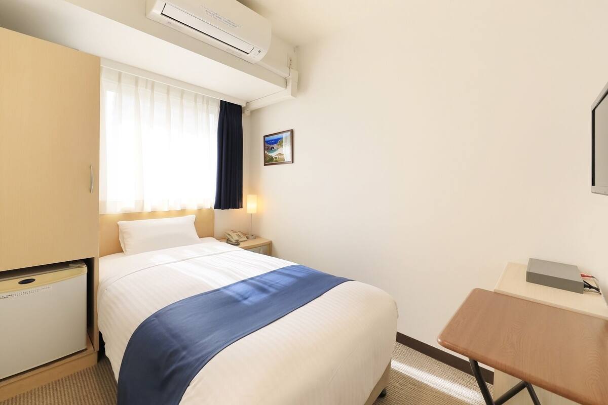 Une chambre d’hôtel équipée d’un lit, d’une table de chevet, d’une lampe, d’un téléviseur, d’un climatiseur et d’un petit bureau.