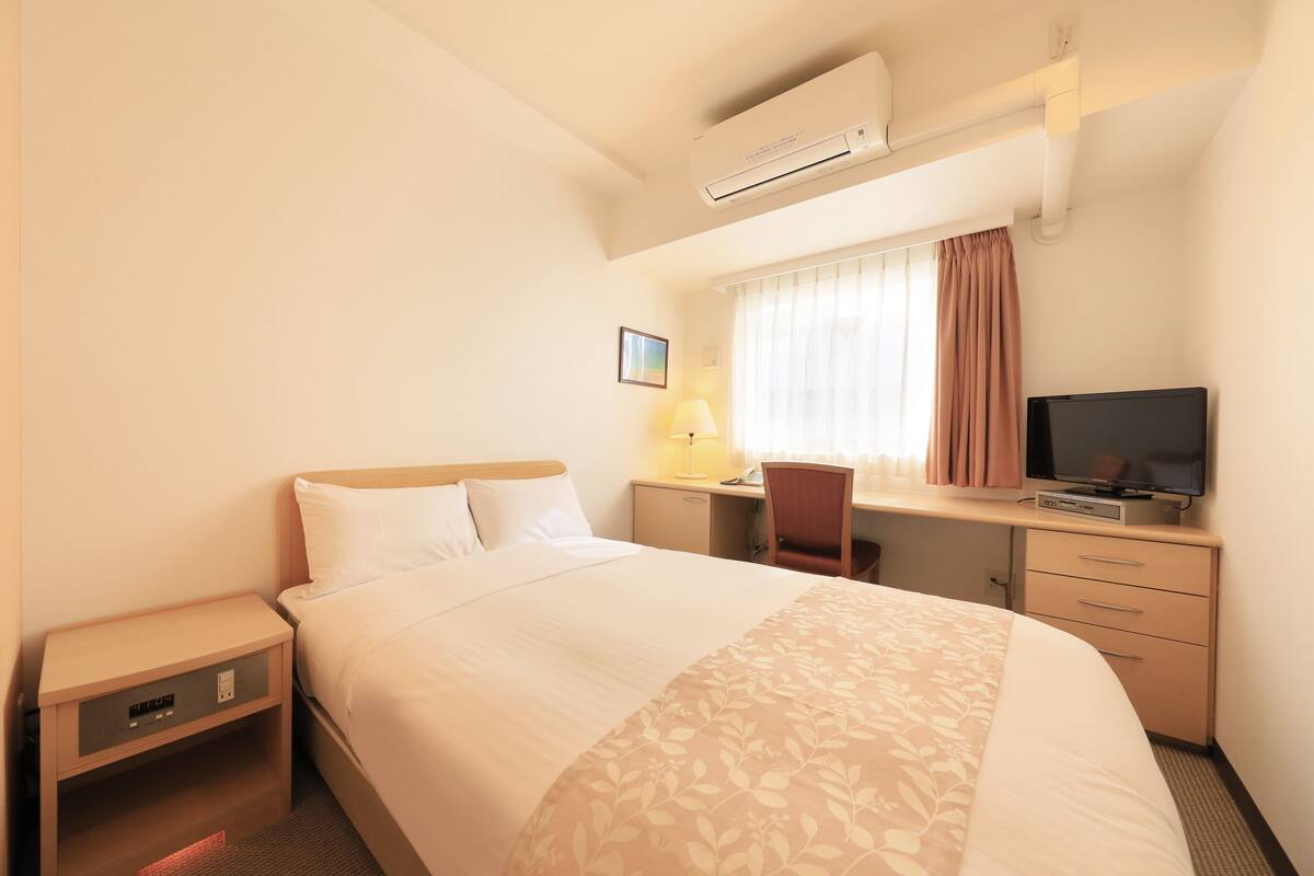 Une chambre d’hôtel équipée d’un lit, d’un bureau, d’une chaise, d’une télévision, d’une lampe et d’un appareil de climatisation.
