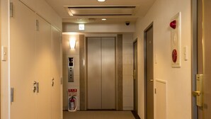 A hotel hallway with carpeted floors, doors on both sides, and an elevator in the center. - Hotel Famy Inn Kinshicho (Tokyo)