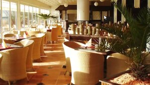 A spacious indoor area with wicker furniture, large windows, and potted plants. - Inselhof Vineta (Zempin)