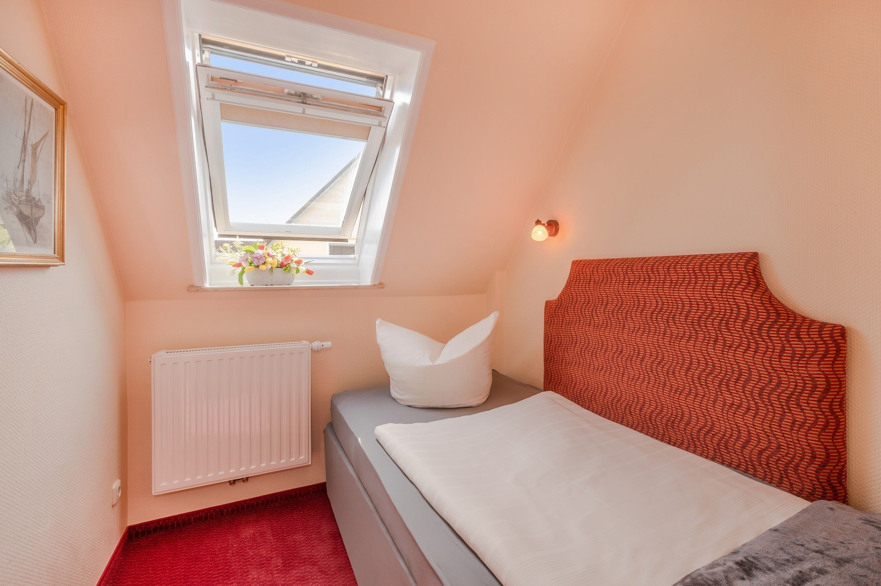 Une chambre à coucher avec un lit, une fenêtre, un radiateur et un luminaire fixé au mur.