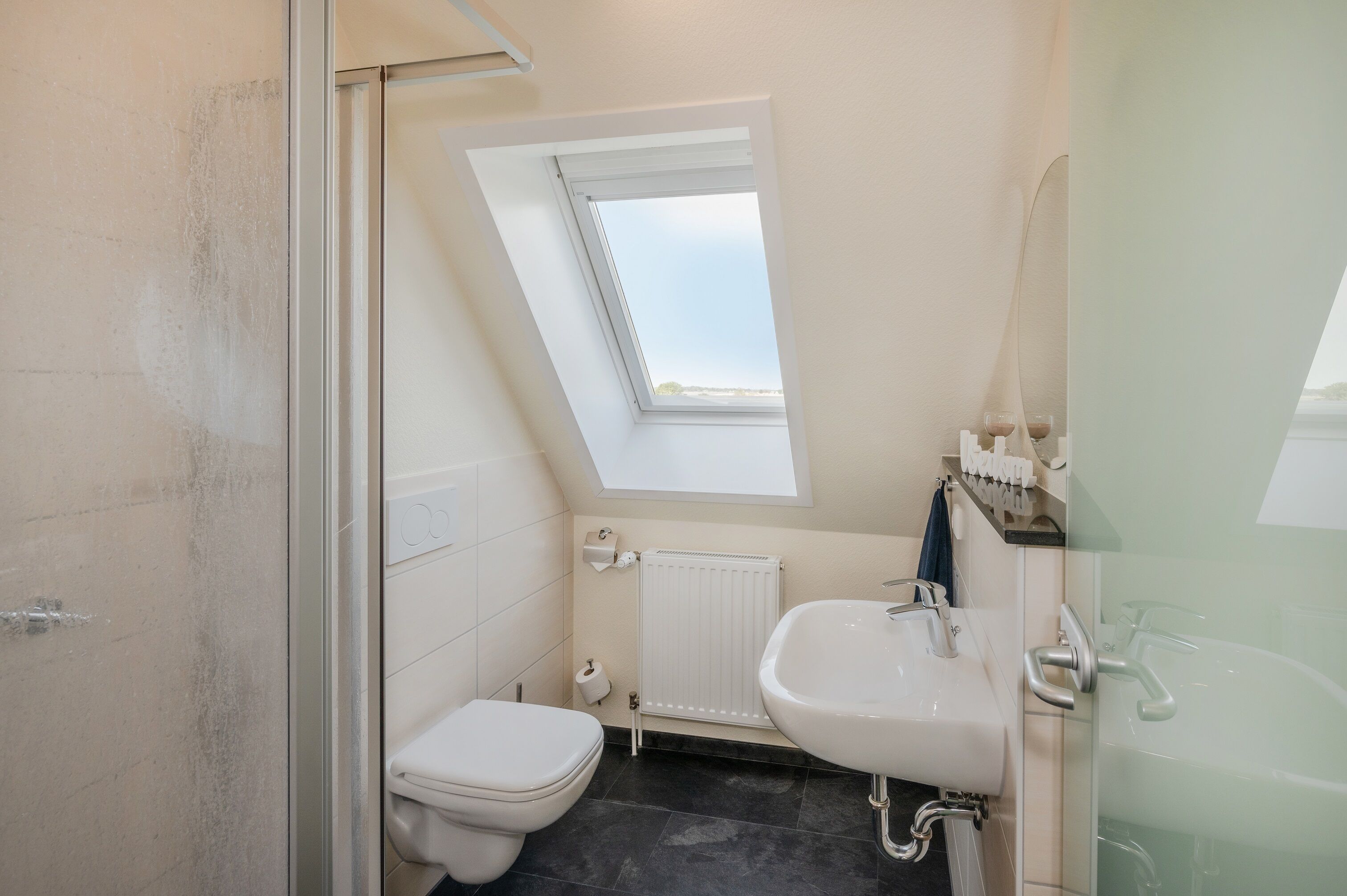 Ein kleines, modernes Badezimmer mit einem Oberlicht, einer Toilette, einem Waschbecken und einer Badewanne.
