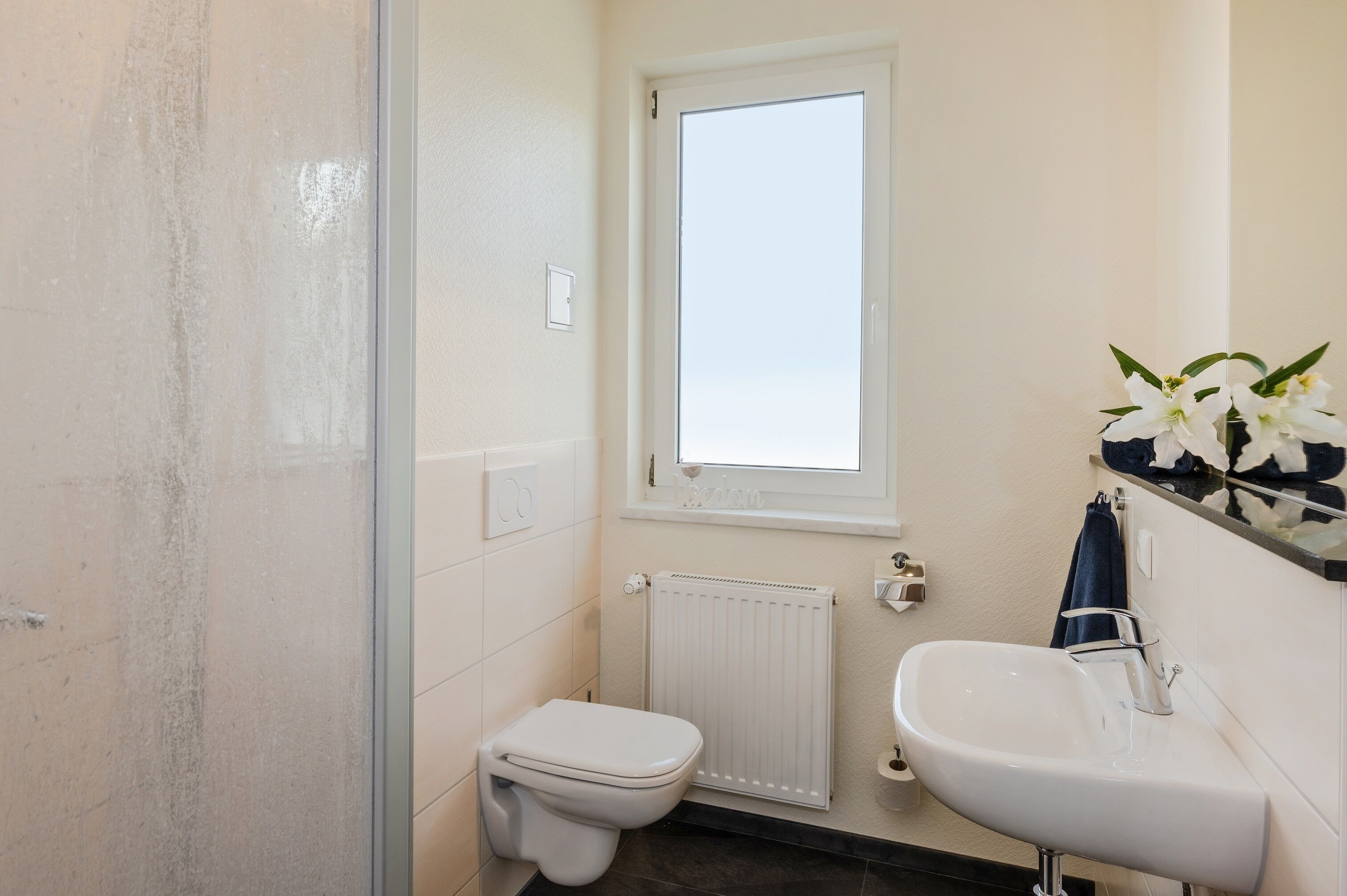 A small bathroom with a toilet, a sink, a window, and a radiator.