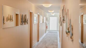 A hotel hallway with wooden floors, beige walls, and framed artwork on the walls.