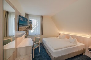Une chambre d’hôtel avec un lit, un bureau, une chaise, une télévision et une fenêtre avec des rideaux.