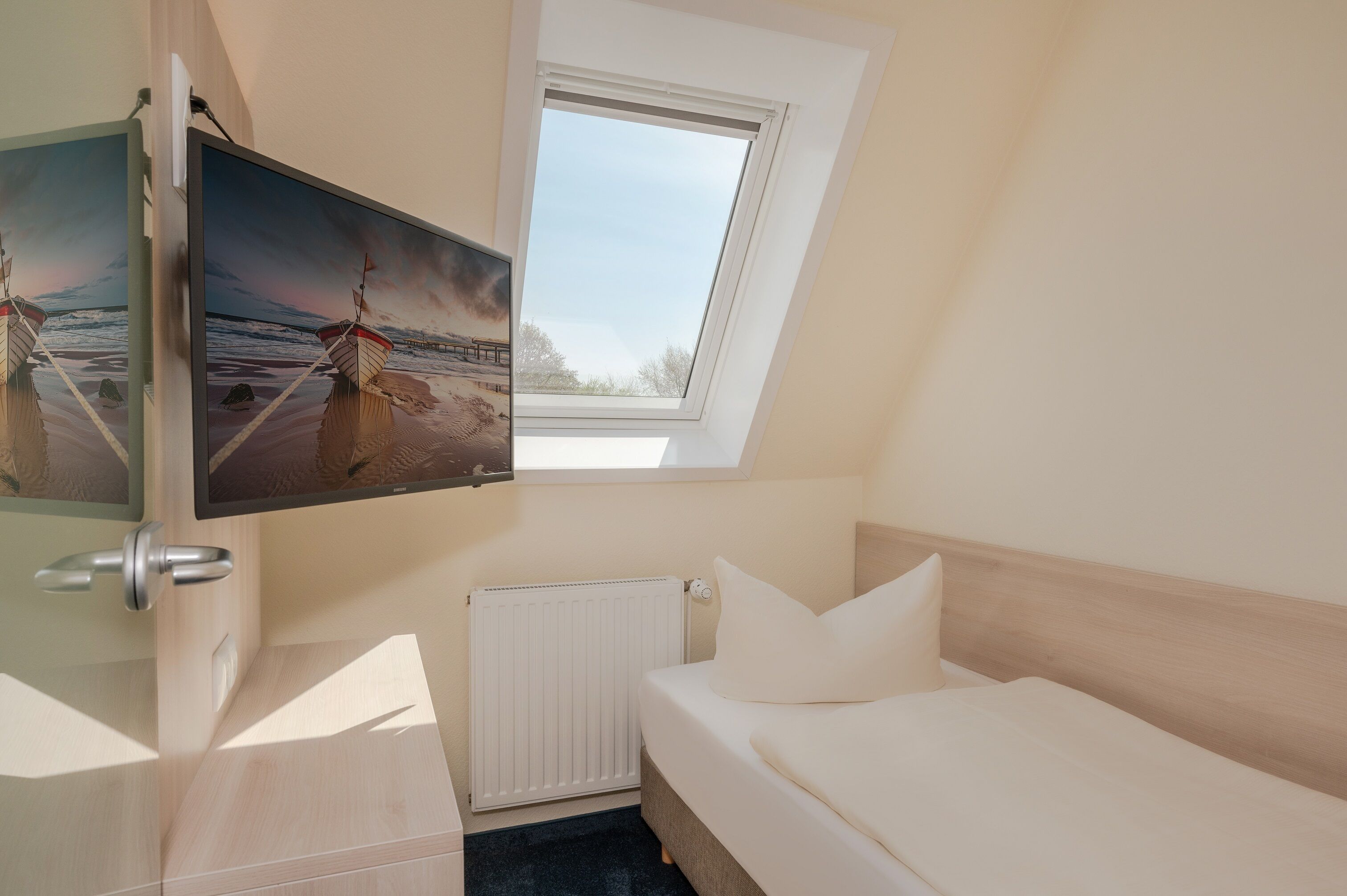 Ein Schlafzimmer mit einem Bett, einem Fenster, einem Heizkörper und einem an der Wand befestigten Fernseher.
