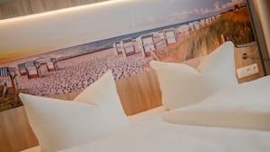 A hotel room with a beach scene mural, white bedding, and a wooden headboard. - Inselhof Vineta (Zempin)