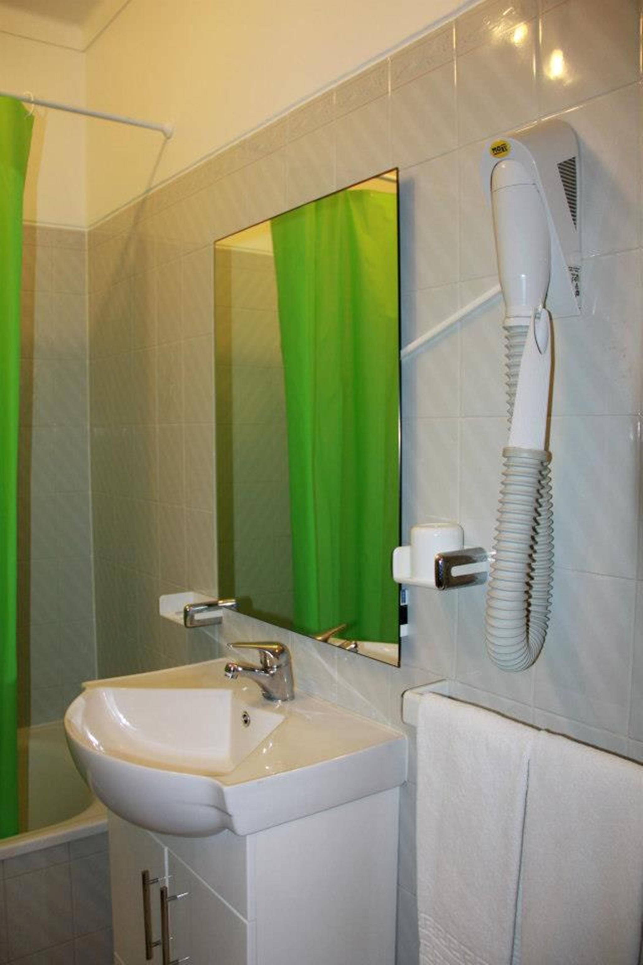 A bathroom with a white sink, a mirror, a hairdryer mounted on the wall, and a green shower curtain.