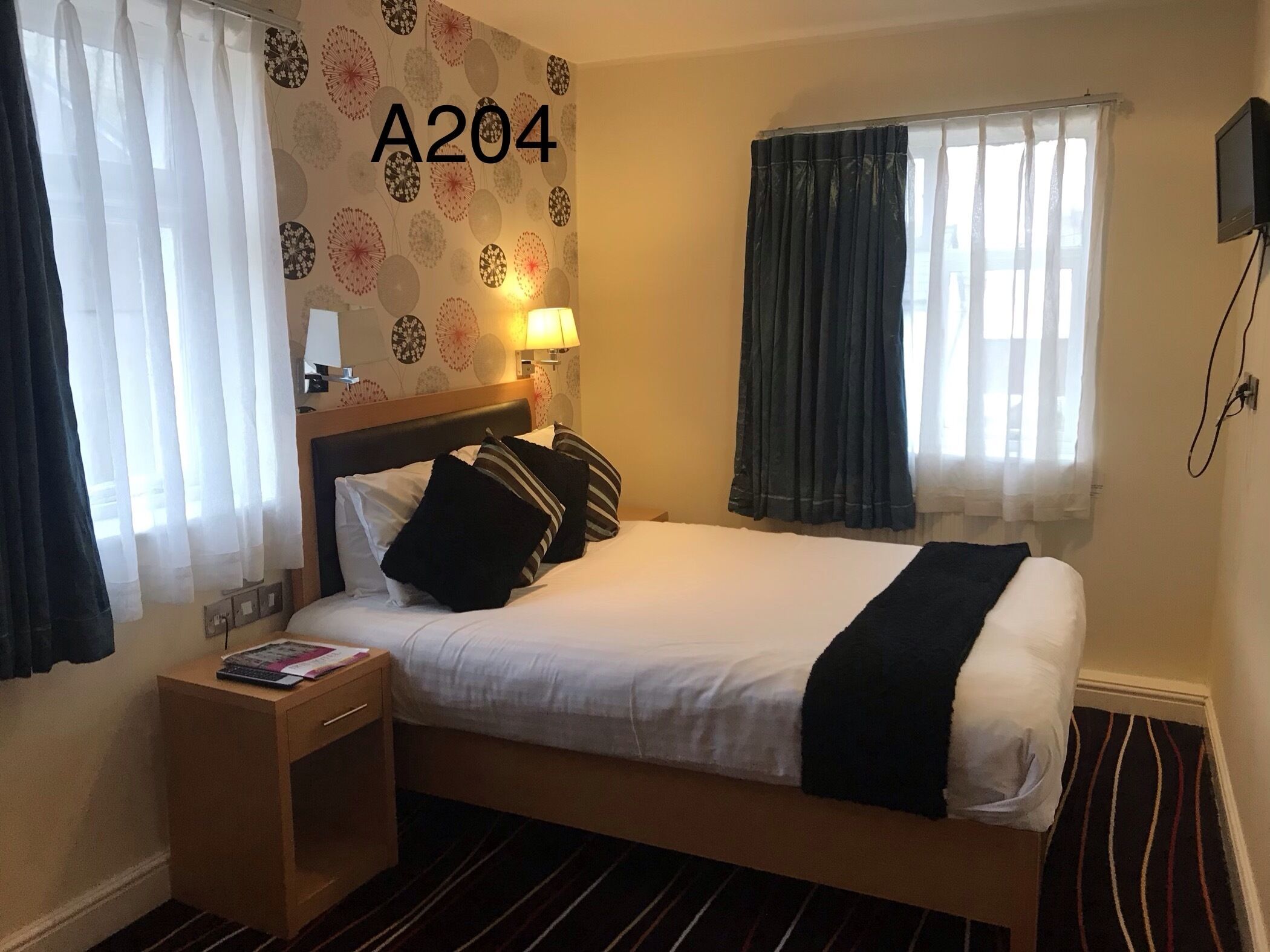 Habitación de hotel con cama, mesita de noche, lámpara y ventana con cortinas.