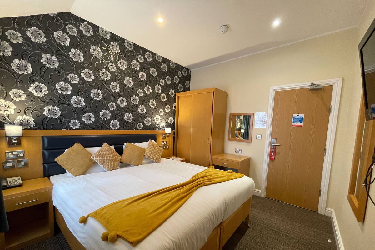 A hotel room with a bed, nightstands, a wardrobe, a mirror, and a door with a fire safety sign.