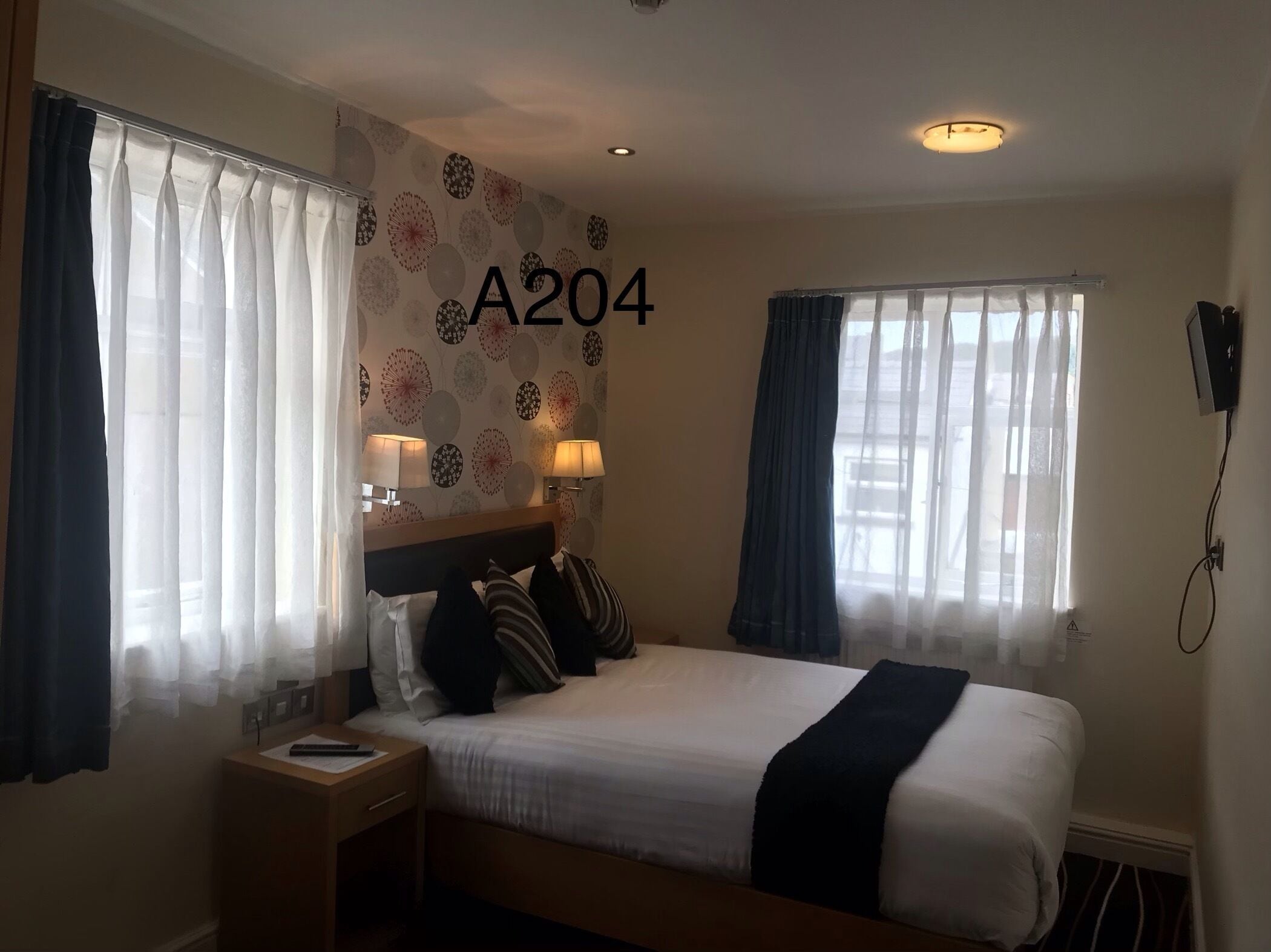 Habitación de hotel con cama, dos lámparas de noche, una mesita de noche y una pared con el número A204.