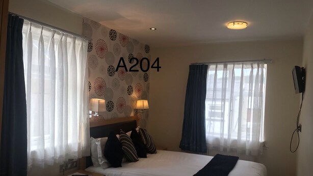 Habitación de hotel con cama, dos lámparas de noche, una mesita de noche y una pared con el número A204.